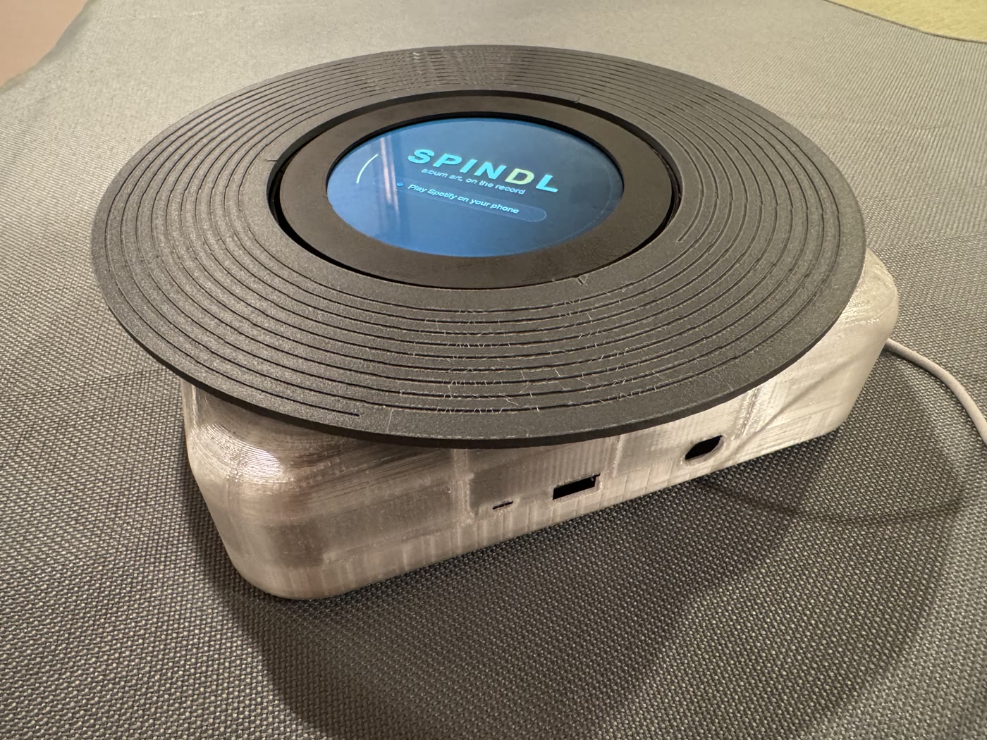 Early SPNDL prototype with a charcoal grooved disc and home screen in a translucent enclosure